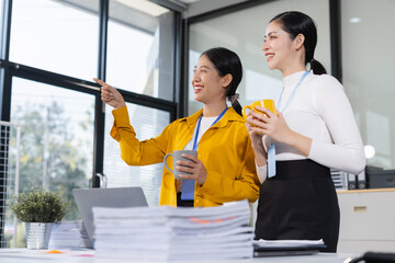 Two young Asian woman colleague descent holds a cup of coffee and talking discussion ideas and...