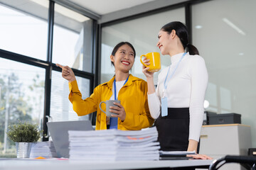 Two young Asian woman colleague descent holds a cup of coffee and talking discussion ideas and...