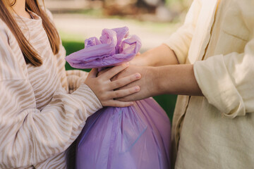 Close-up of mother and daughter's hands collecting waste in disposable trash bag on the public...