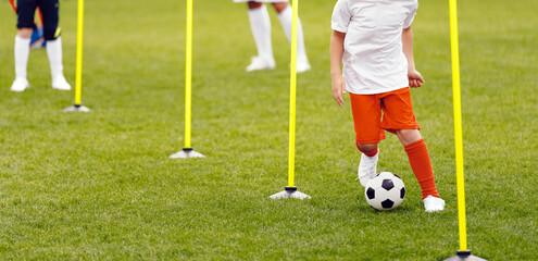 Young athlete running with soccer ball in slalom between agility poles. Soccer education for kids....
