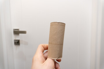Man's hand taking an empty toilet paper in a WC. Empty toilet paper roll in hand. Man's hand holding brown paper tube close-up. 