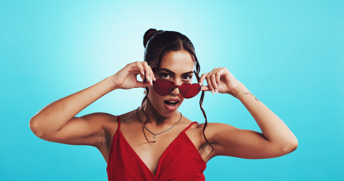 Portrait, woman and heart sunglasses for fashion, style or trendy emoji isolated on blue studio background. Love, shades or girl with cool accessory, romance or confident model on valentines holiday