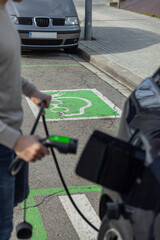 Close-up of an unrecognizable man plugging in an electric car at a public EV charging spot. Green...