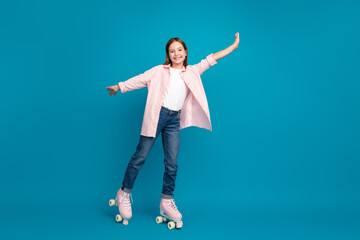 Young girl in casual pink shirt and jeans roller skating against a vivid blue studio background