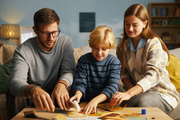 Family sitting in living room engaging in creative crafting activity with young child eagerly...