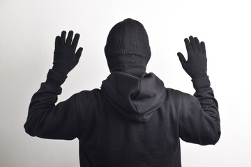 Back of Thief wearing black jacket and mask caught with hands raised, isolated on white background.