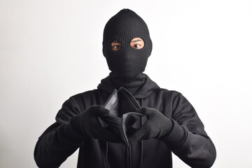 Thief wearing black jacket and mask checking his stolen empty wallet, isolated on white background.