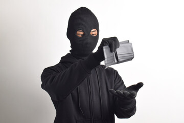 Thief wearing black jacket and mask checking his stolen empty wallet, isolated on white background.