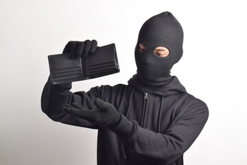 Thief wearing black jacket and mask checking his stolen empty wallet, isolated on white background.