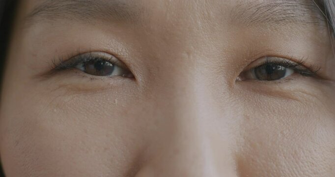 Close-up of young Asian woman's eyes looking at camera blinking with no emotion. Human body part and vision concept.