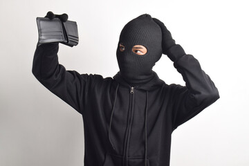 Thief wearing black jacket and mask checking his stolen empty wallet, isolated on white background.