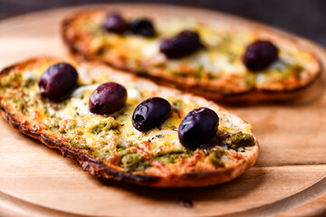 Bruschetta with mozzarella and cheddar cheese, olive pesto and kalamata olives. on wooden background. Soft focus. Close up