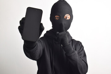 Mysterious man wearing black hoodie and mask doing hacking activity on smartphone, putting finger...