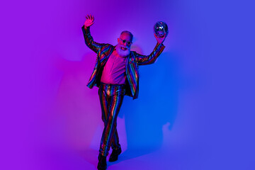 Full size photo of macho senior male hold disco ball dressed colorful sequins striped garment isolated on blue purple neon light background
