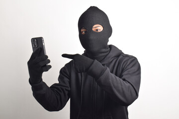 Mysterious man wearing black hoodie and mask doing hacking activity on smartphone, finger pointing...