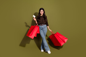 Young woman with red shopping bags and credit card against khaki background expressing leisure and joy