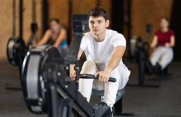 Guy exercises on a rowing machine in the gym. European man is preparing for the rowing competition....