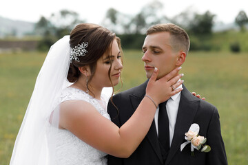 A woman in a white wedding dress and a veil decorated with a shiny hairpin gently holds the chin of...