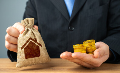 Businessman holding a bag with a house symbol and money coins. Sale of building permits. Housing...