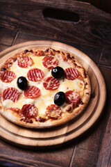 Pizza with salami, mozzarella and cheddar cheese. Wooden background. Soft focus. Close up.