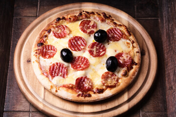 Pizza with salami, mozzarella and cheddar cheese. Wooden background. Soft focus. Close up.