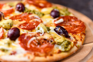 Pizza with chorizo ​​sausage, mozzarella and cheddar cheese, olive pesto and kalamata olives. Wooden background. Soft focus. Close up.
