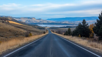 Serene landscape featuring an empty road winding through hills and mountains under a blue sky
