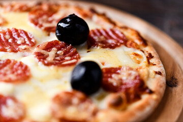 Pizza with salami, mozzarella and cheddar cheese. Wooden background. Soft focus. Close up.