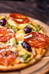 Pizza with chorizo ​​sausage, mozzarella and cheddar cheese, olive pesto and kalamata olives. Wooden background. Soft focus. Close up.