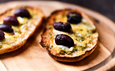 Bruschetta with mozzarella and cheddar cheese, olive pesto and kalamata olives on wooden background. Soft focus. Close up