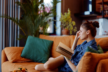 Obraz premium Cozy evening at home woman sitting on a couch with a book and a glass of wine