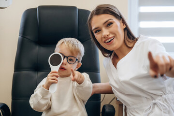Sitting with doctor. Little boy is having check up in the ophthalmologist cabinet