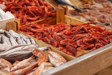 Vibrant red shrimp displayed on ice in a wooden crate at a seafood market, surrounded by various fresh fish, creating a colorful and appetizing seafood selection
