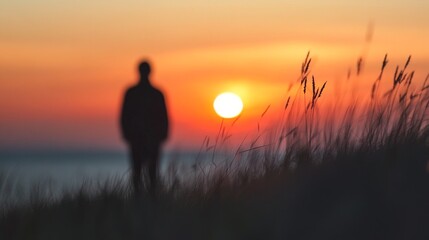 Fototapeta premium Silhouette of a person standing on a grassy shore during a vibrant sunset over the ocean