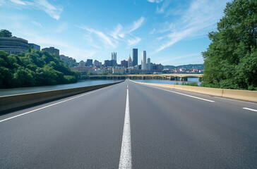 A wide road leads to the city skyline, overlooking the river with trees on both sides. The asphalt surface is clean and smooth, with white lines at its edge