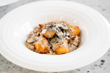 A gourmet plate featuring crispy fried fish fillets topped with creamy mushroom sauce, served on a bed of bulgur wheat in an elegant white bowl.