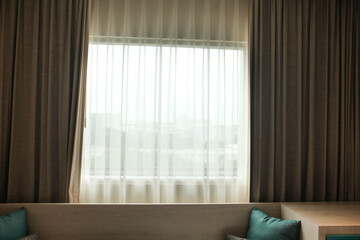 A hotel window with brown curtains and a sheer white drape, creating a warm and elegant atmosphere