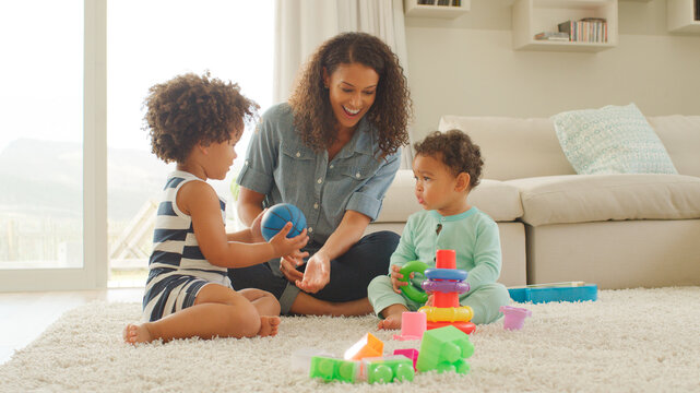 Mother Sits With Children At Home Playing With Plastic Stacking Toys