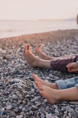 Family relaxation time by the beach with bare feet on rocky shore in the evening light