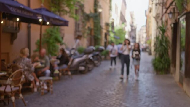Blurry street scene in rome italy featuring outdoor cafes with people dining under umbrellas and pedestrians walking past on cobblestone streets with greenery and old buildings around.