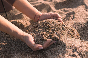Hands releasing beach sand during sunset on a tranquil shoreline