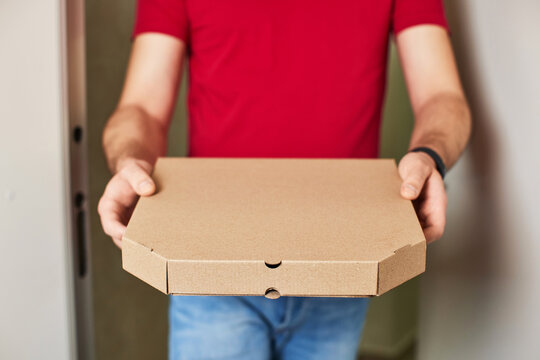 delivery man in red t-shirt giving food order and holding pizza box at home, close-up