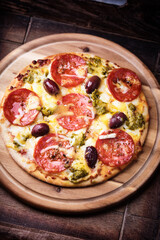 Pizza with chorizo ​​sausage, mozzarella and cheddar cheese, olive pesto and kalamata olives. Wooden background. Soft focus. Close up.	