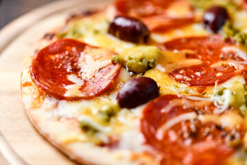 Pizza with chorizo ​​sausage, mozzarella and cheddar cheese, olive pesto and kalamata olives. Wooden background. Soft focus. Close up.	