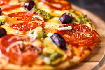 Pizza with chorizo ​​sausage, mozzarella and cheddar cheese, olive pesto and kalamata olives. Wooden background. Soft focus. Close up.	