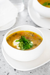 A close-up of a creamy soup in a white bowl, garnished with fresh herbs. The soup features a vibrant mix of vegetables, showcasing a cozy and inviting meal.