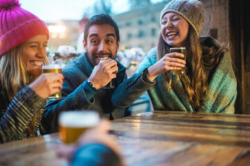 Young friends having fun together drinking craft beers at pub restaurant - Winter lifestyle and party concept - Main focus on right girl hand
