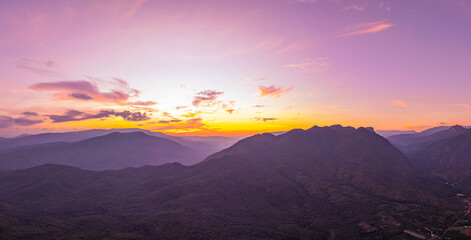 A breathtaking view of a colorful sunset over layered mountain silhouettes, with warm hues of orange, pink, and blue blending seamlessly across the sky.