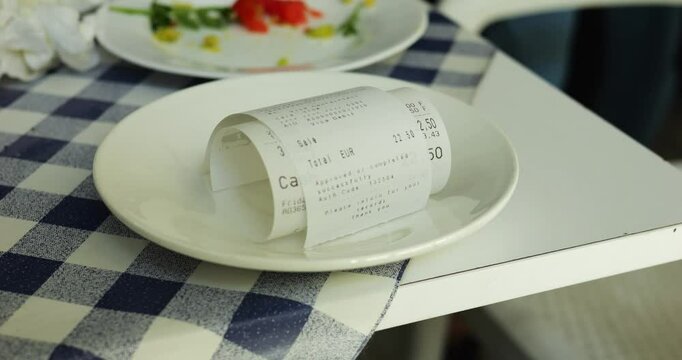 Rolled up check for meal in canteen lies on small plate in dining room. Special paper bill contains information about cost of dishes and total amount