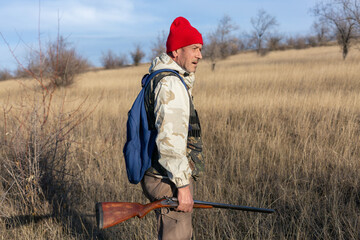 Mature hunter man holding a shotgun and walking through a field